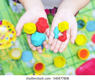 Close-up of a child's hands playing with colorful playdough and textured rollers
