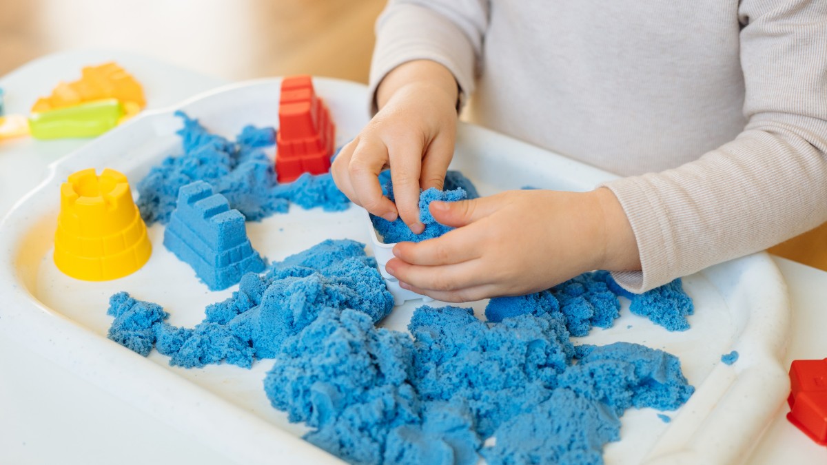 Close-up of a child's hands playing with kinetic sand and textured sensory balls