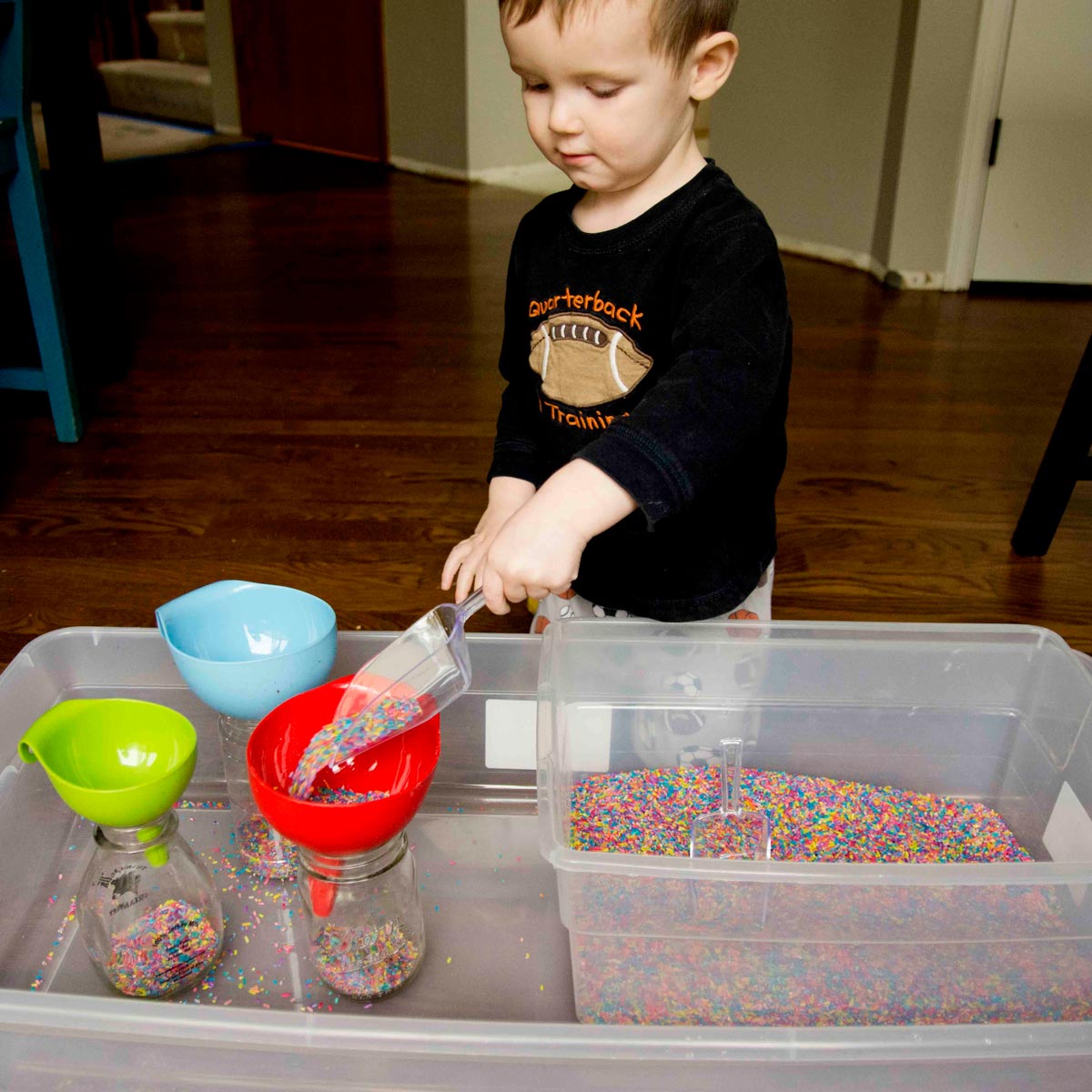 Toddler playing with sensory bin filled with colored rice and scoops