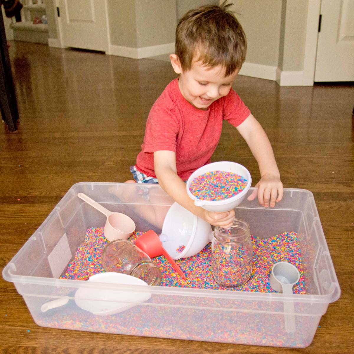 Sensory bin filled with colored rice, scoops, and figurines